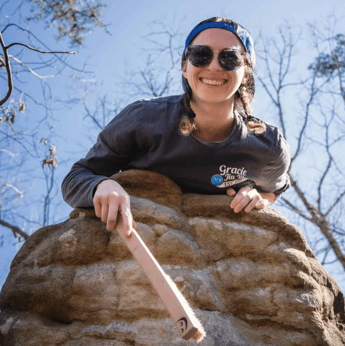 A woman smiling while holding a bat on a rock.